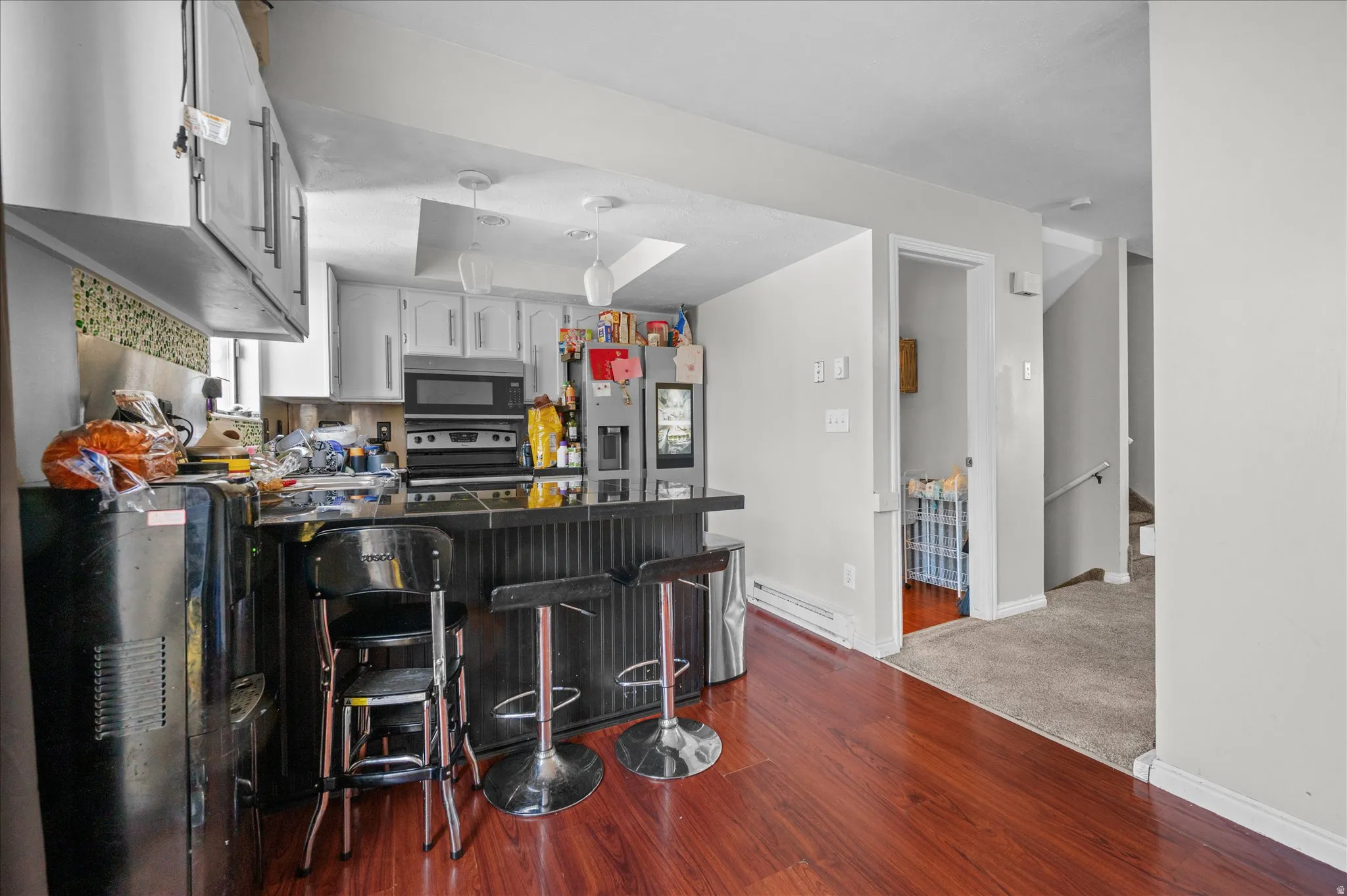 Kitchen with dark countertops, a peninsula, a kitchen breakfast bar, white cabinetry, and dark wood-style flooring