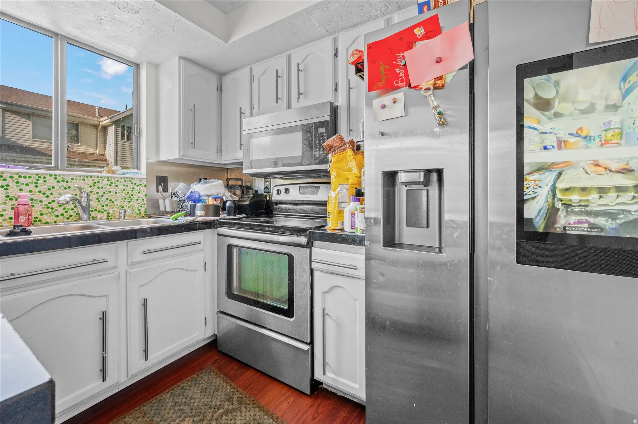 Kitchen featuring stainless steel appliances, white cabinetry, dark wood-style flooring, and tasteful backsplash