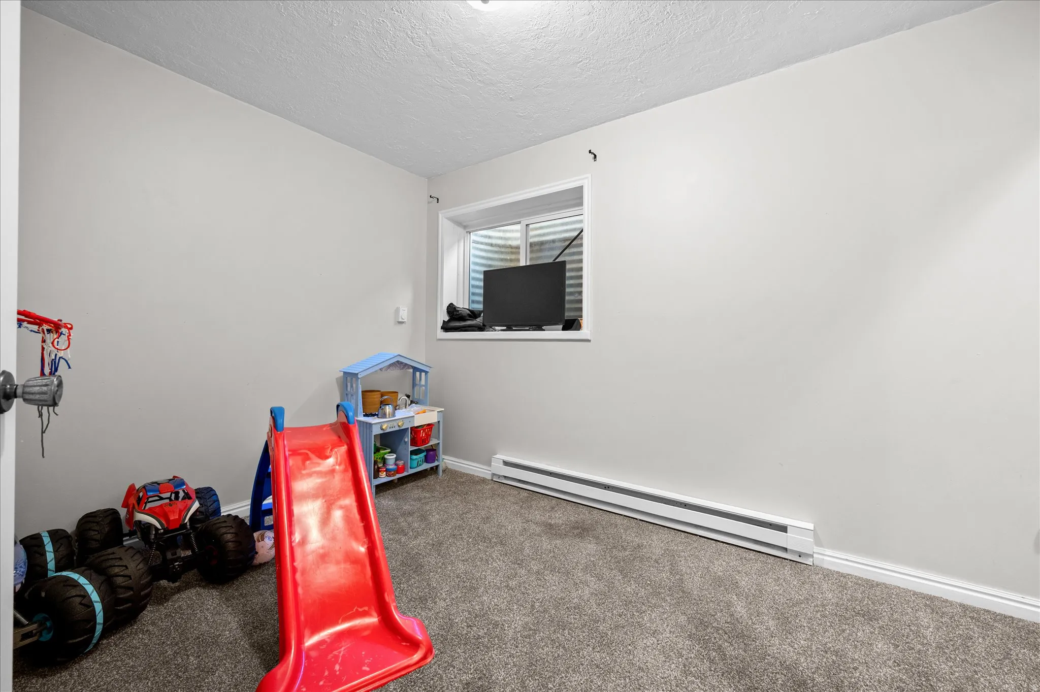 Recreation room with a baseboard heating unit, carpet flooring, and a textured ceiling