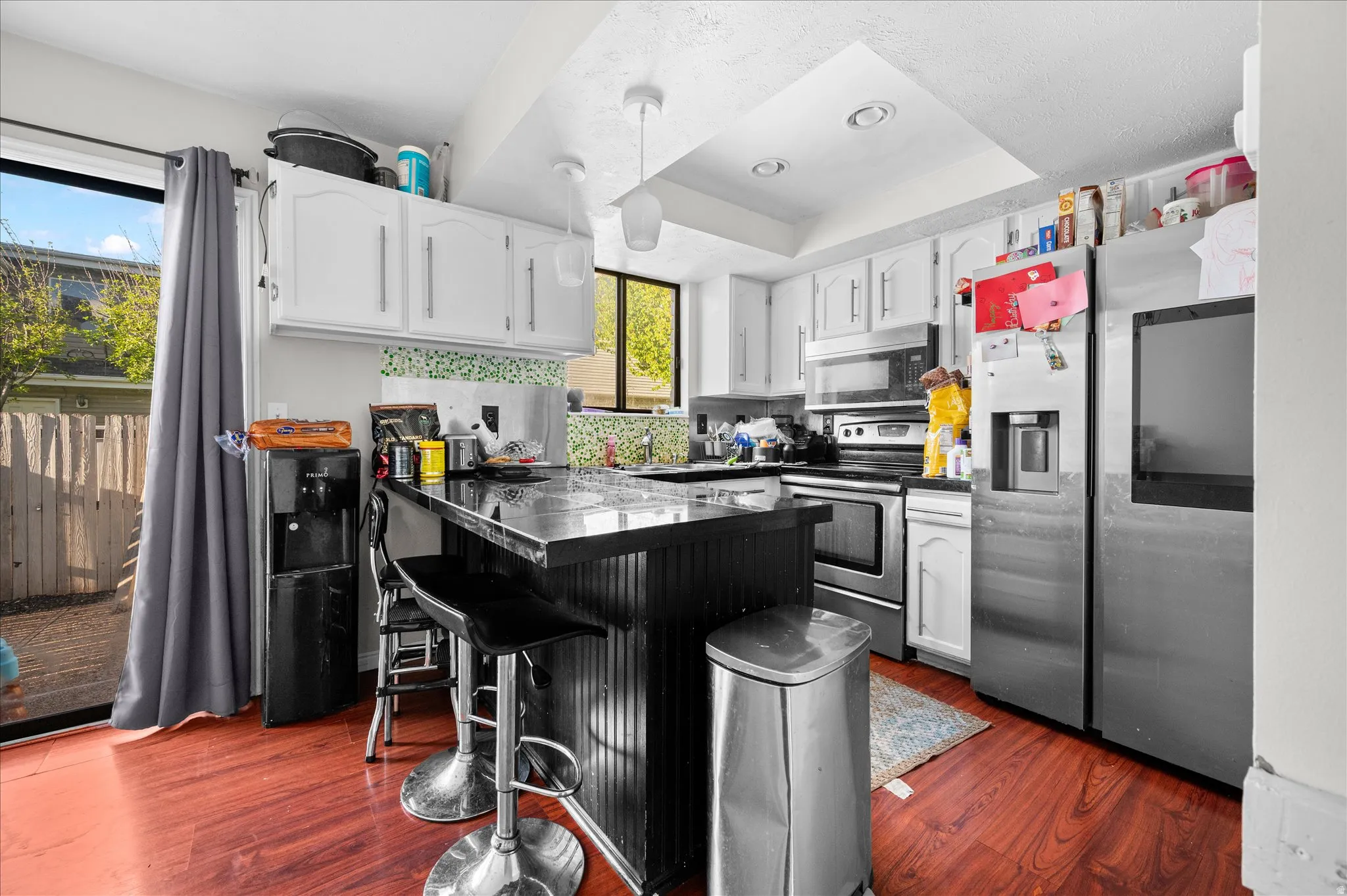 Kitchen with dark countertops, white cabinets, stainless steel appliances, a raised ceiling, and a peninsula