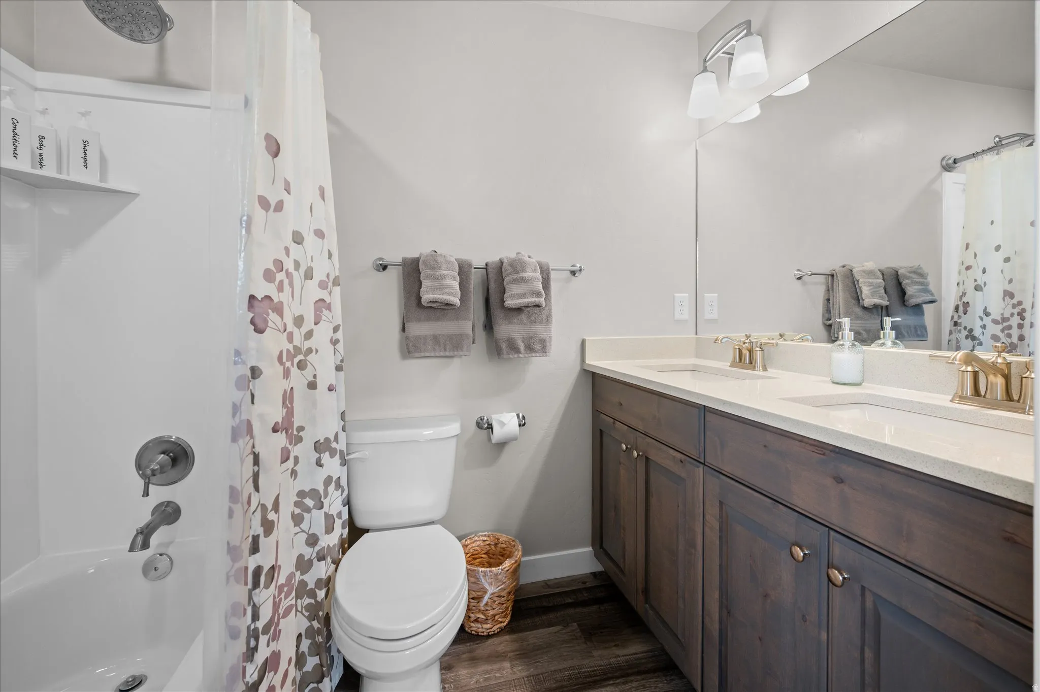 Full bath featuring double vanity, dark wood-style flooring, and shower / tub combo