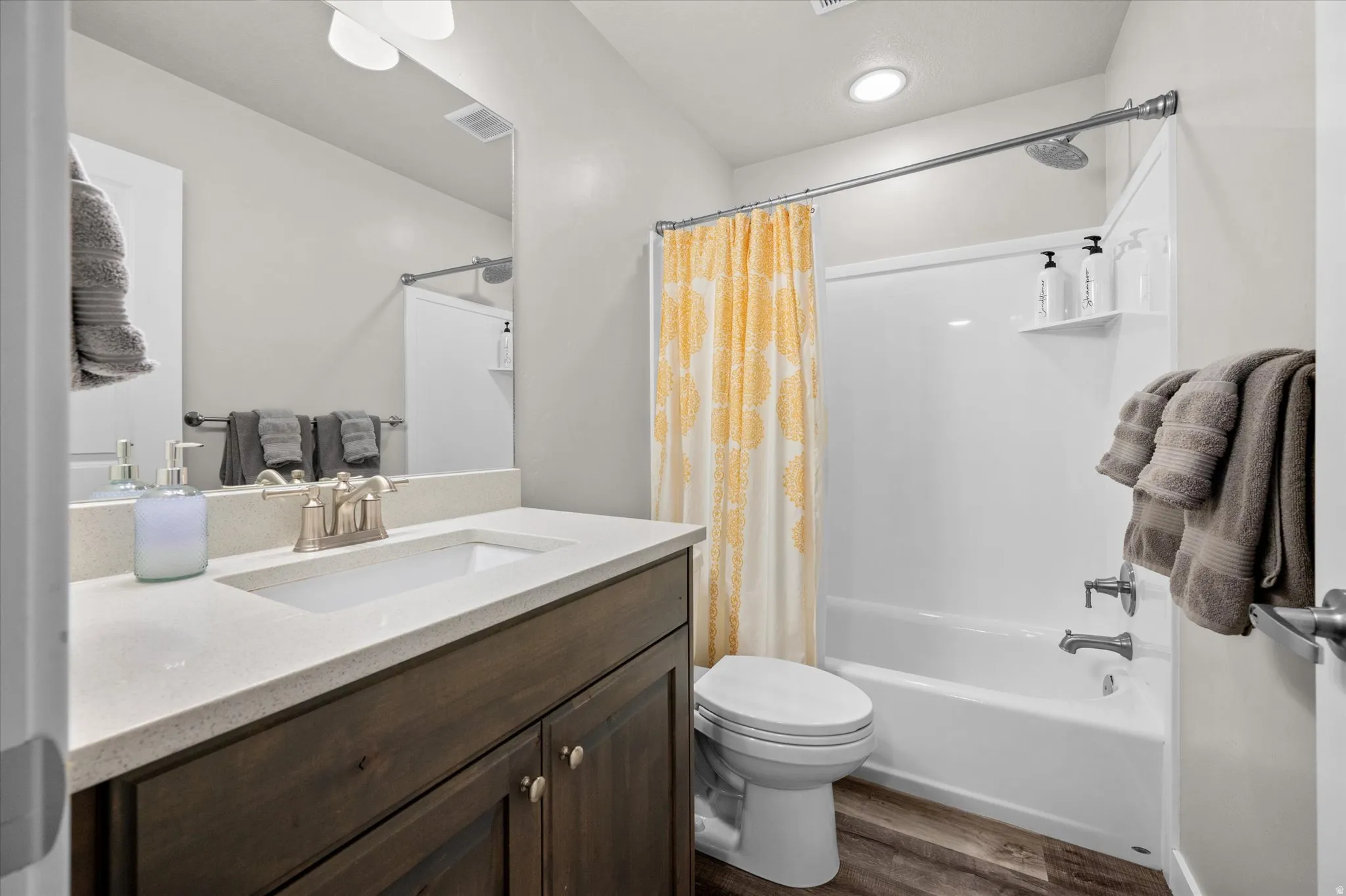 Bathroom featuring vanity, shower / bathtub combination with curtain, and dark wood-type flooring