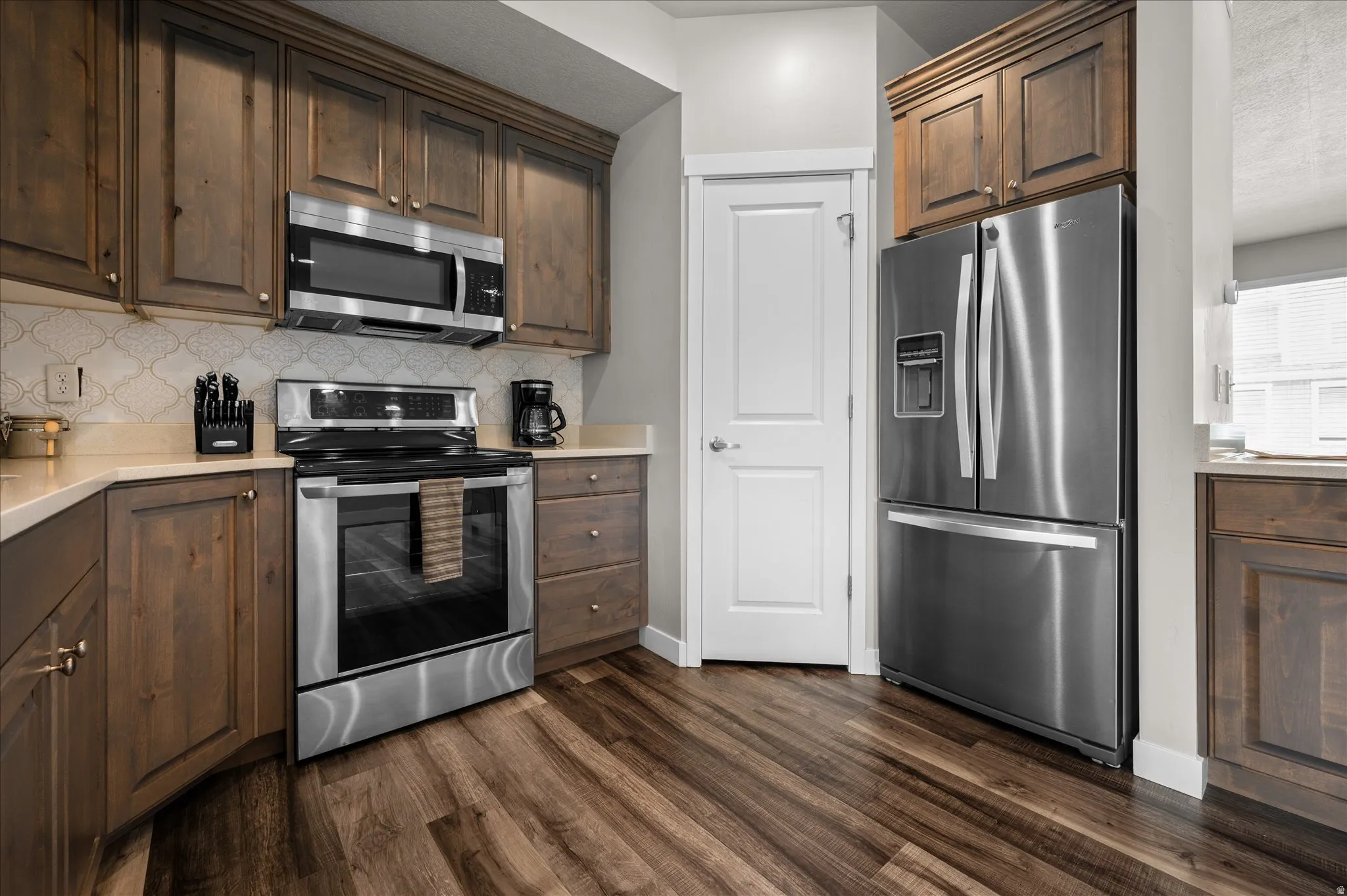 Kitchen featuring stainless steel appliances, dark wood finish cabinetry, dark wood-type flooring, tasteful backsplash, and light stone counters