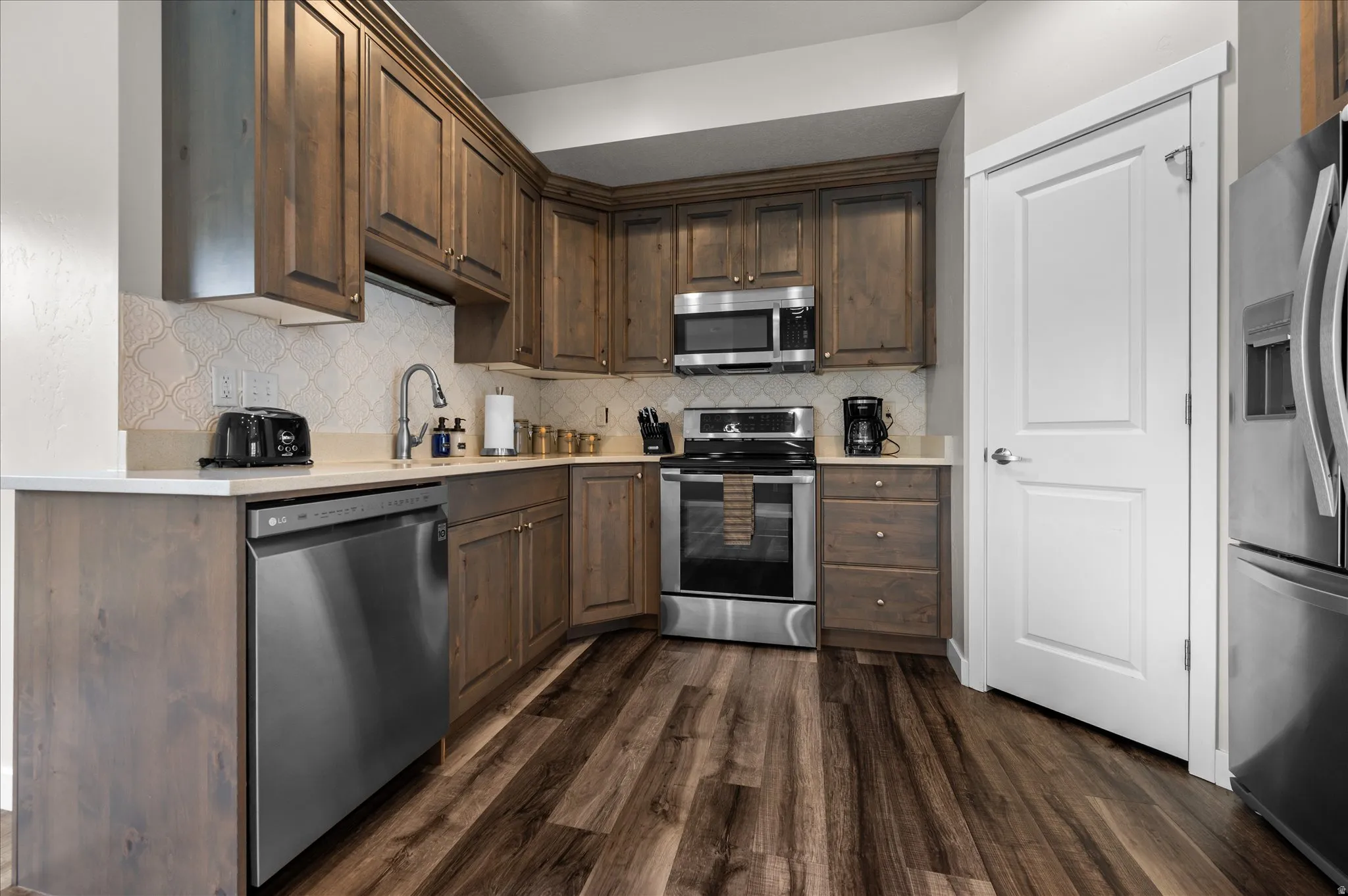 Kitchen with stainless steel appliances, dark wood finish cabinetry, dark wood-type flooring, and backsplash