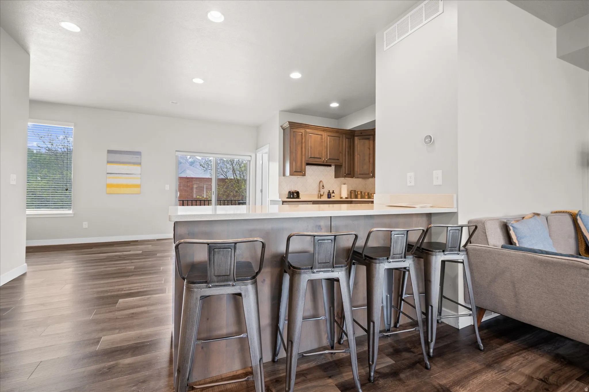 Kitchen featuring a peninsula, light countertops, open floor plan, a breakfast bar area, and dark wood-style flooring