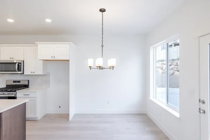 White shaker cabinetry, stainless steel appliances, tile backsplash, wood-finish flooring, and a contemporary chandelier