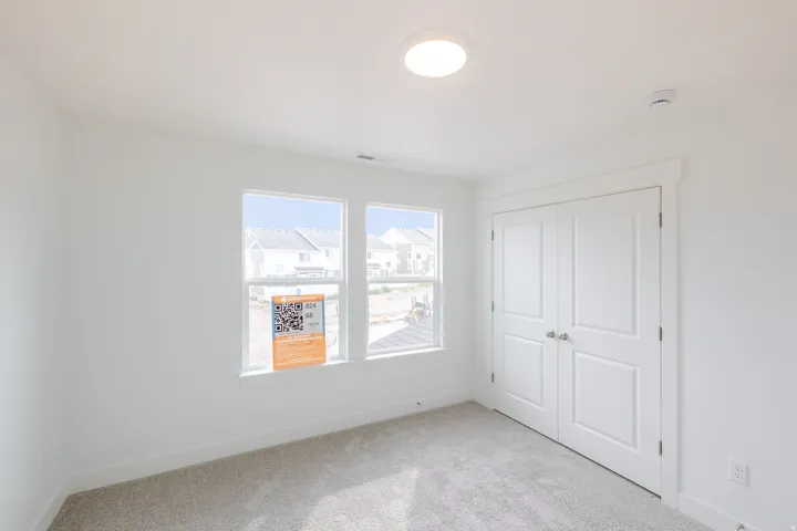 Light-filled room featuring two windows, neutral carpeting, and a double-door closet with paneling