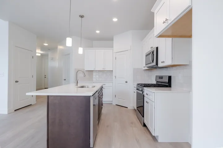 Kitchen island with an undermount sink, white countertops, stainless steel appliances, and white cabinetry with a tile backsplash