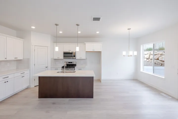 White cabinetry, light wood-finish flooring, central island with an integrated sink, stainless steel appliances, and a modern chandelier