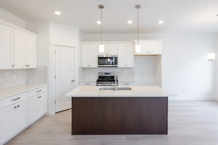 Contemporary kitchen featuring white cabinetry, a central island with a contrasting base, stainless steel appliances, and light wood-finish flooring