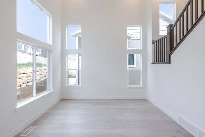 High ceilings with multiple large windows, light wood-finish flooring, and a dark wood staircase with balusters