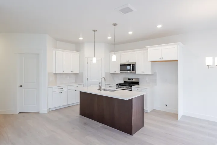 Expansive kitchen with a central island, white cabinetry, integrated stainless steel appliances, and wood-finish flooring