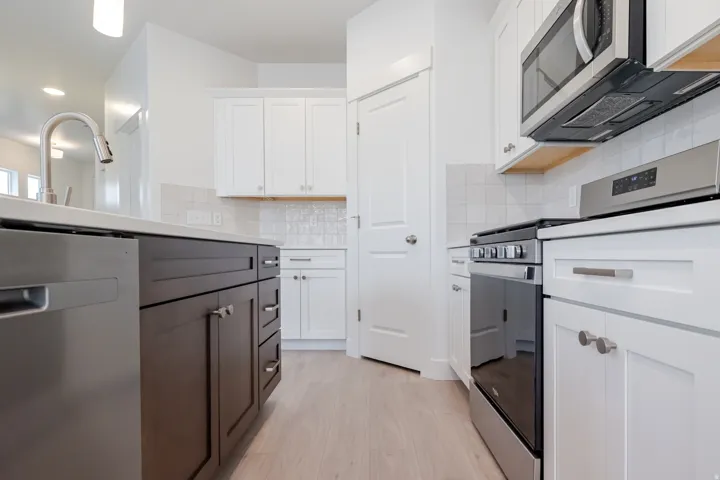 Kitchen featuring stainless steel appliances, two-tone cabinetry, light-toned wood-finish flooring, and white tile backsplash