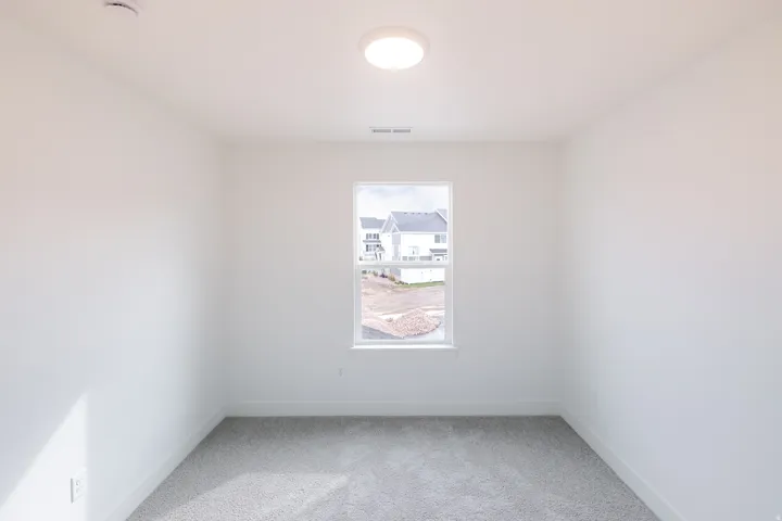 Recessed ceiling light, neutral wall paint, gray carpeting, single window with white trim, electrical outlet
