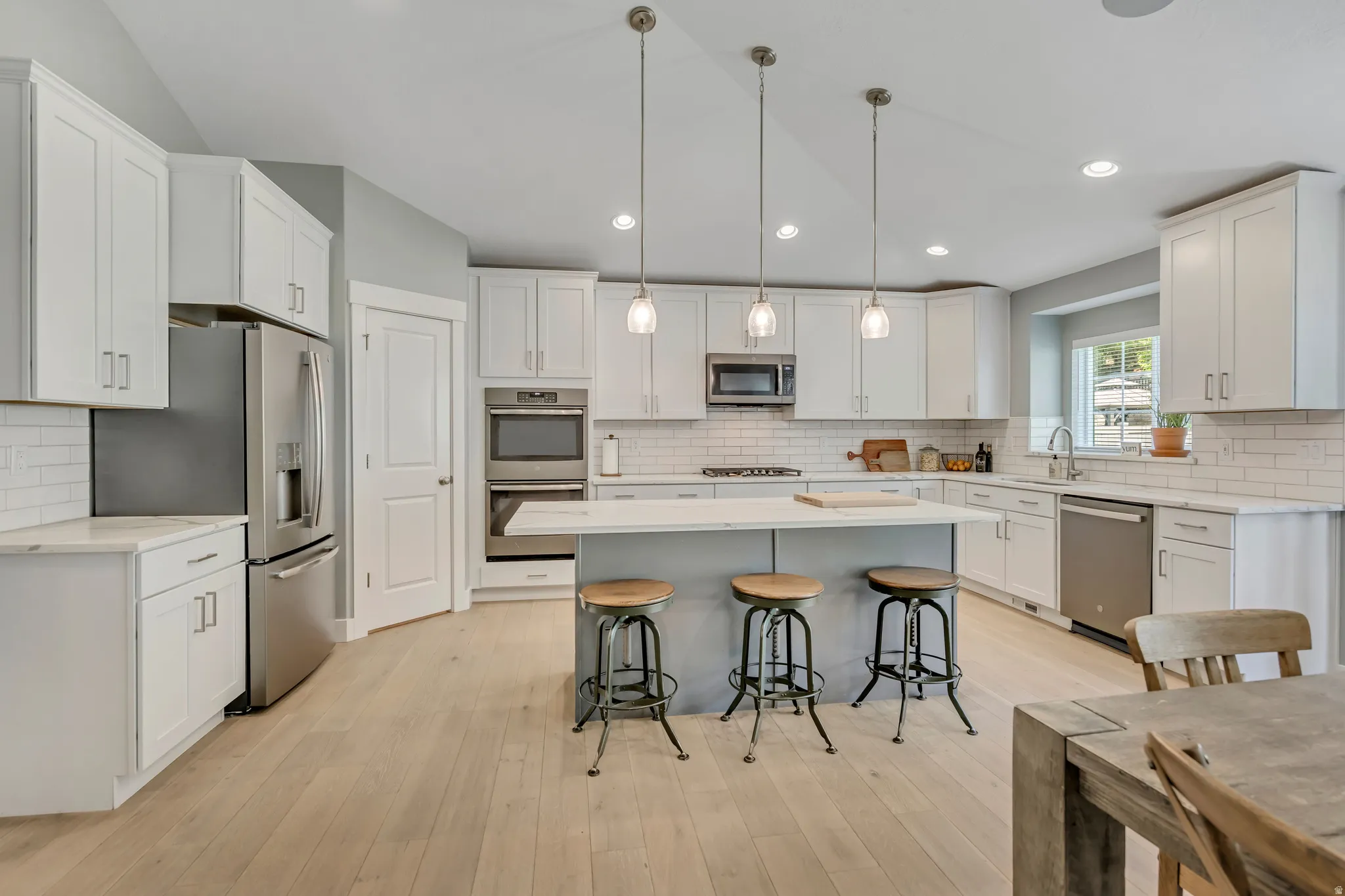 Kitchen with a breakfast bar, stainless steel appliances, decorative light fixtures, white cabinetry, and a kitchen island