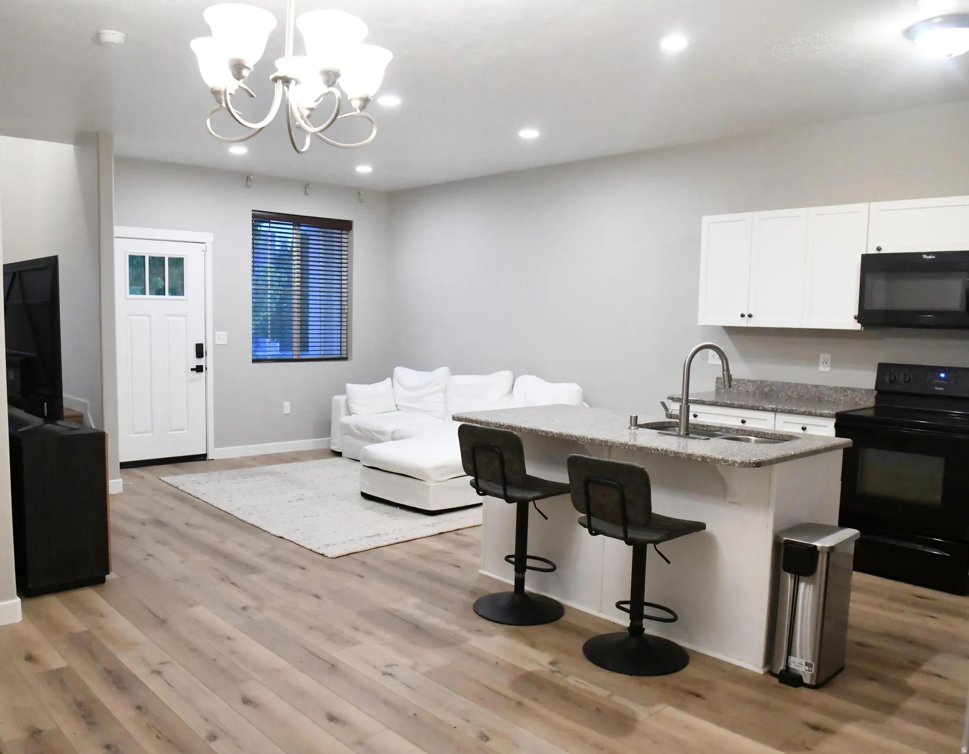 Kitchen with black appliances, white cabinetry, a breakfast bar, light stone countertops, and light wood-style flooring