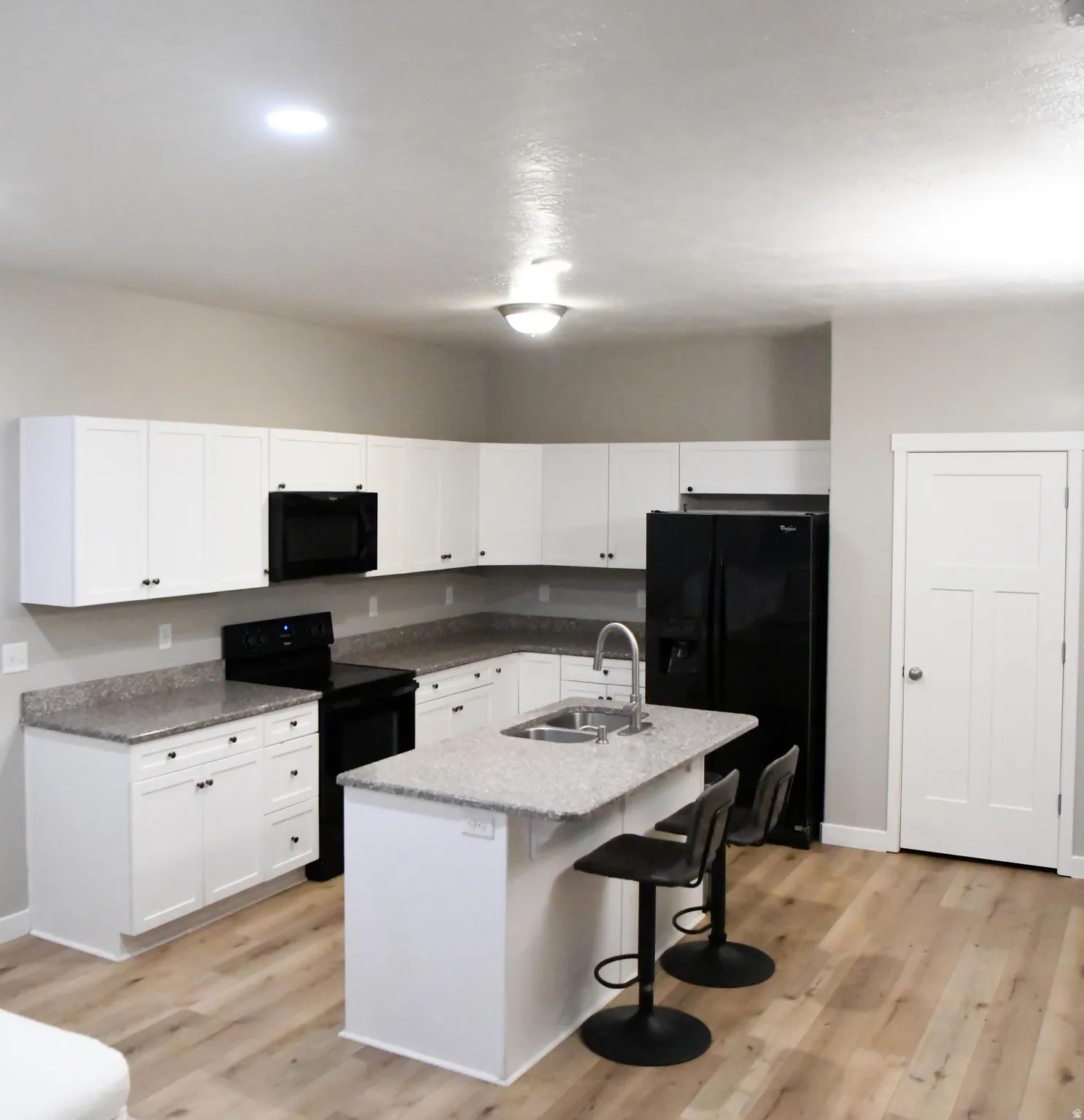 Kitchen with black appliances, white cabinets, a kitchen breakfast bar, a center island with sink, and light wood-style flooring