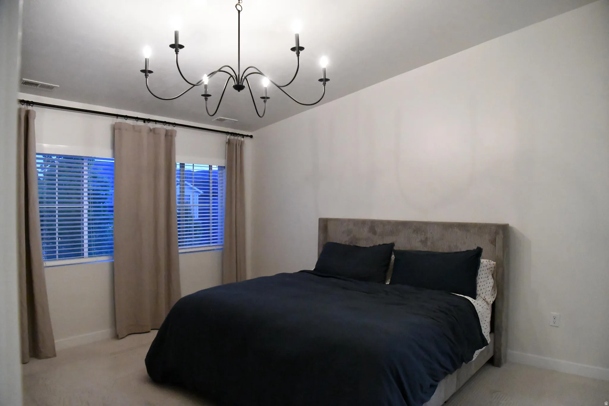 Primary bedroom with light carpet and hanging lights