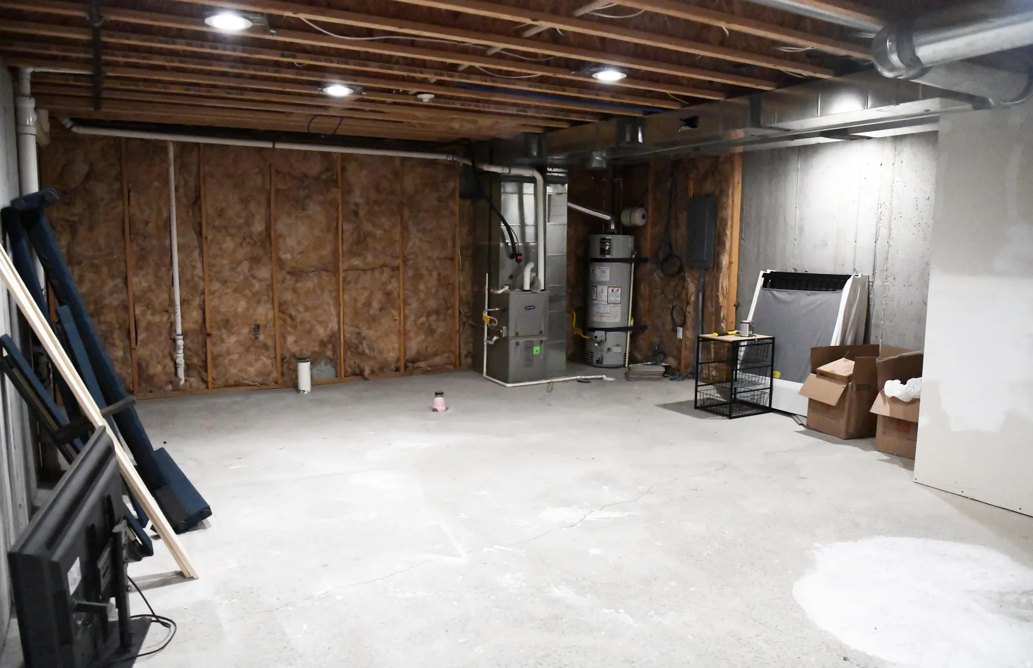 Unfinished basement featuring secured water heater, heating unit, and electric panel