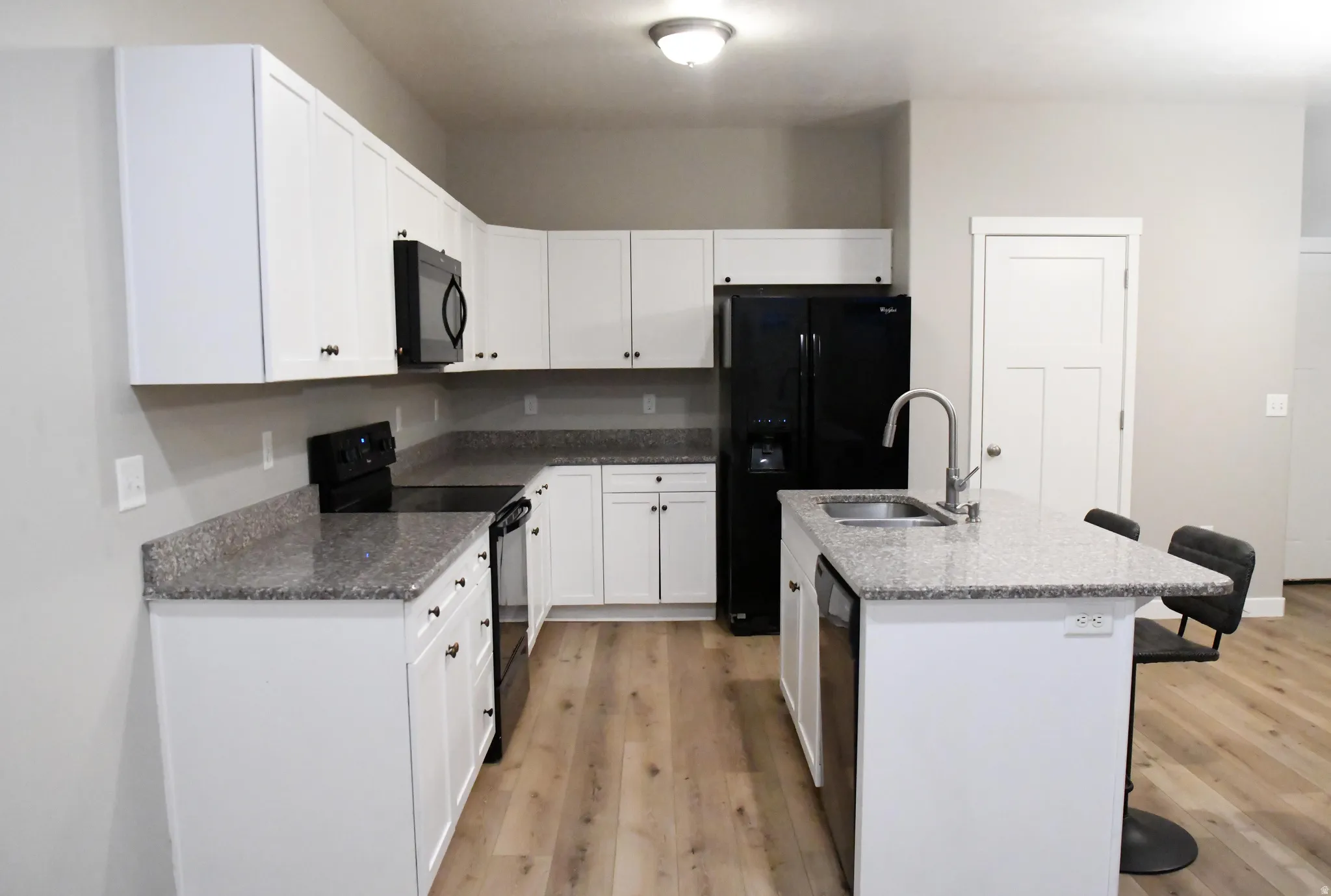 Kitchen featuring a breakfast bar area, black appliances, a kitchen island with sink, light wood-type flooring, and dark stone countertops