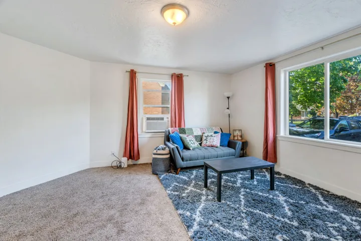 Carpeted living room with healthy amount of natural light and cooling unit.