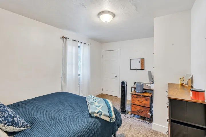 Bedroom with light carpet, a desk, and a textured ceiling.
