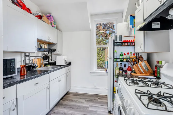 Kitchen featuring white appliances, ventilation hood, white cabinets, light wood-type flooring, and vaulted ceiling.
