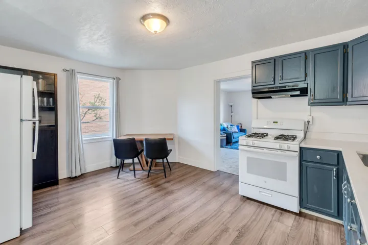 Kitchen featuring white appliances, light countertops, light wood flooring and blue cabinets.