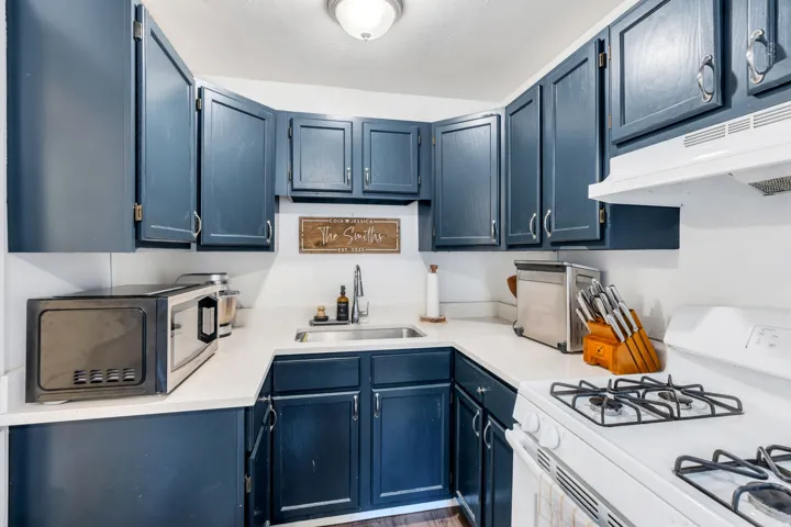 Kitchen with white gas range, blue cabinets, stainless steel microwave, and wood finished floors.