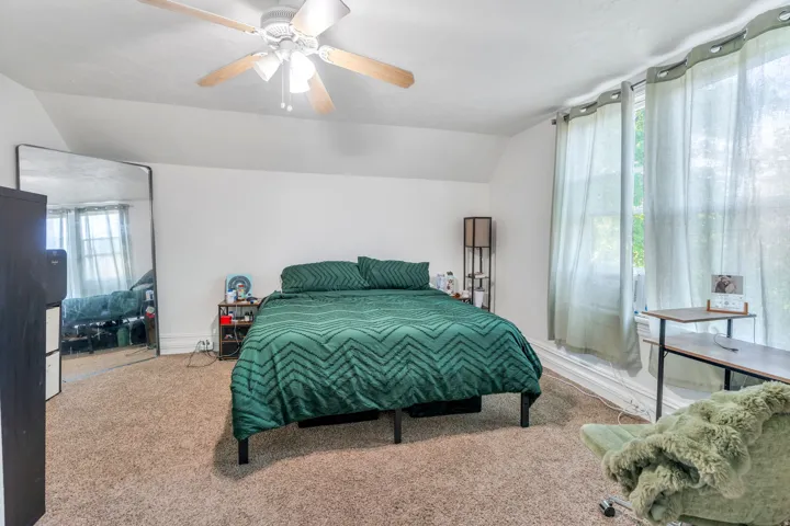 Bedroom with vaulted ceiling, carpet floors, and ceiling fan.