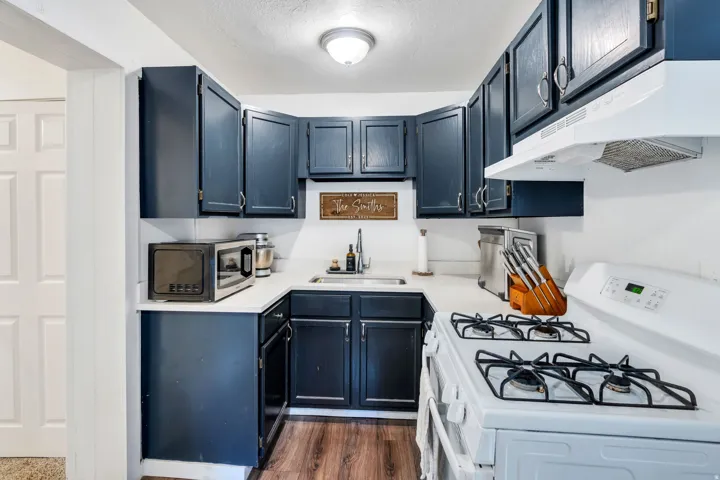 Kitchen with white gas range, light countertops, stainless steel microwave, dark wood-type flooring, and a textured ceiling.