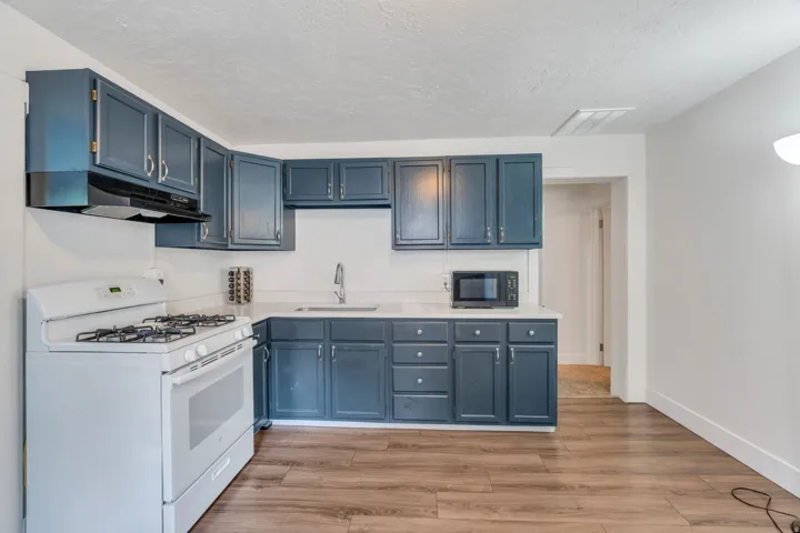 Kitchen with white range with gas cooktop, light wood finished floors, blue cabinetry.