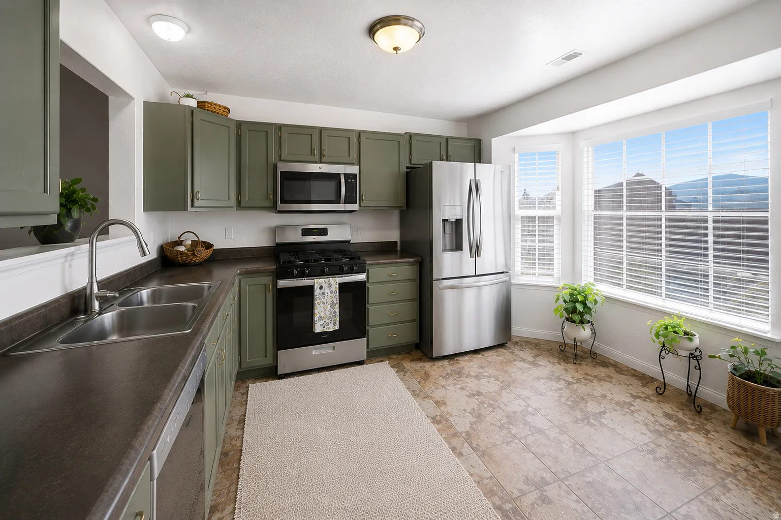 Kitchen featuring green cabinetry, stainless steel appliances, a double basin sink, ample countertop space, and a bay window