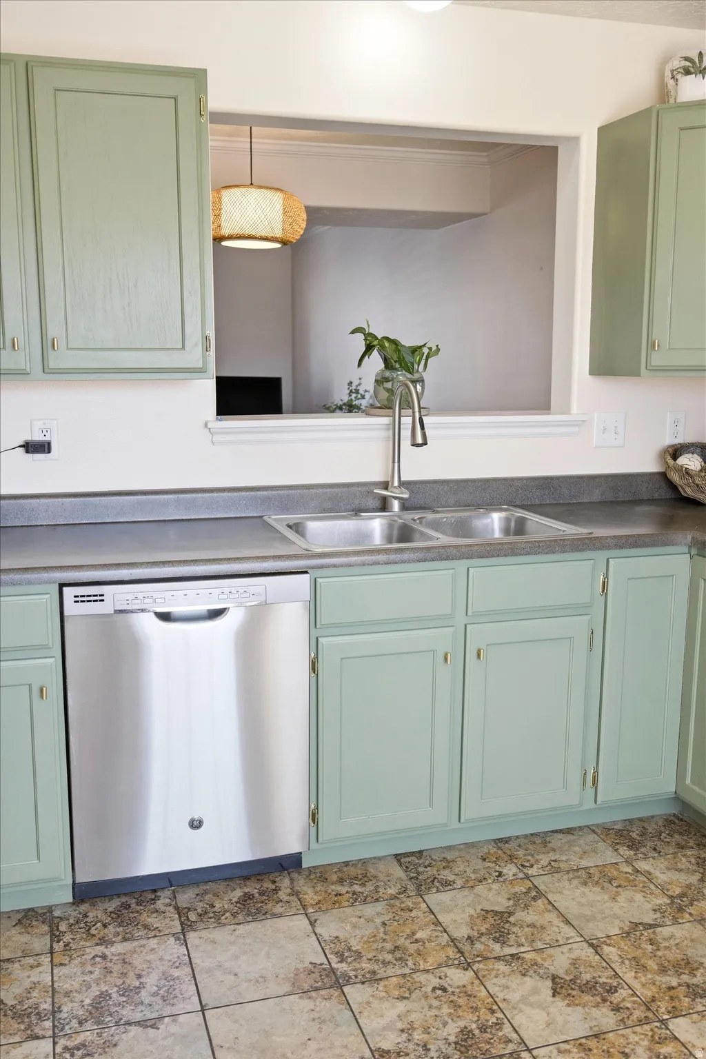 Kitchen with green cabinets, stainless steel dishwasher, and light stone finish flooring