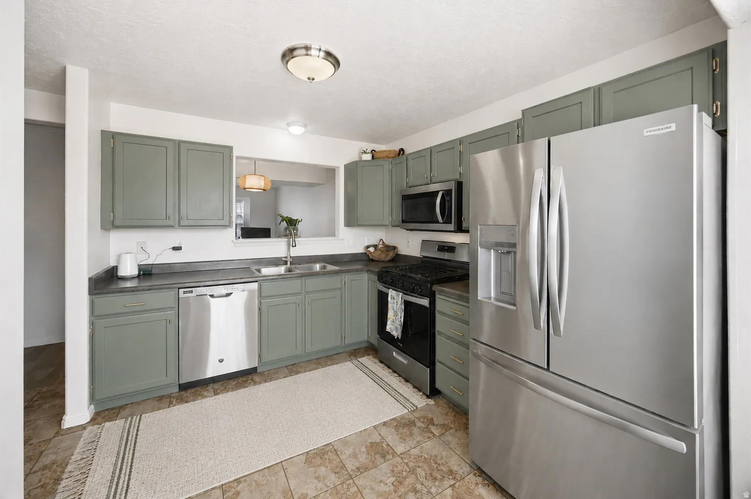 Kitchen featuring sage-toned cabinetry, stainless steel appliances, dark countertops, a double basin sink, and tile flooring