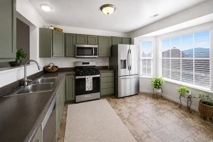 Kitchen featuring green cabinetry, stainless steel appliances, a double basin sink, ample countertop space, and a bay window
