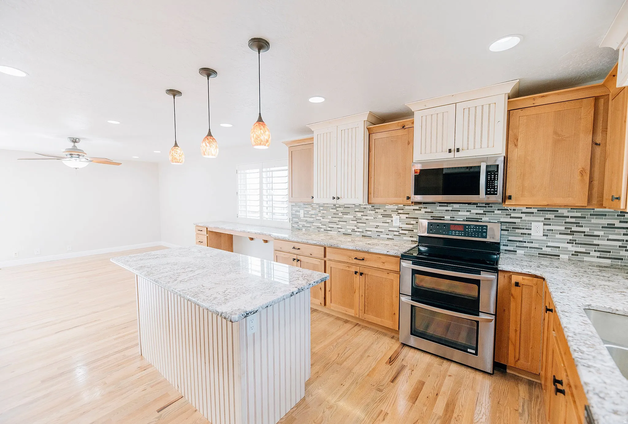 Kitchen featuring stainless steel appliances, light wood finish cabinets, light stone counters, and a center island