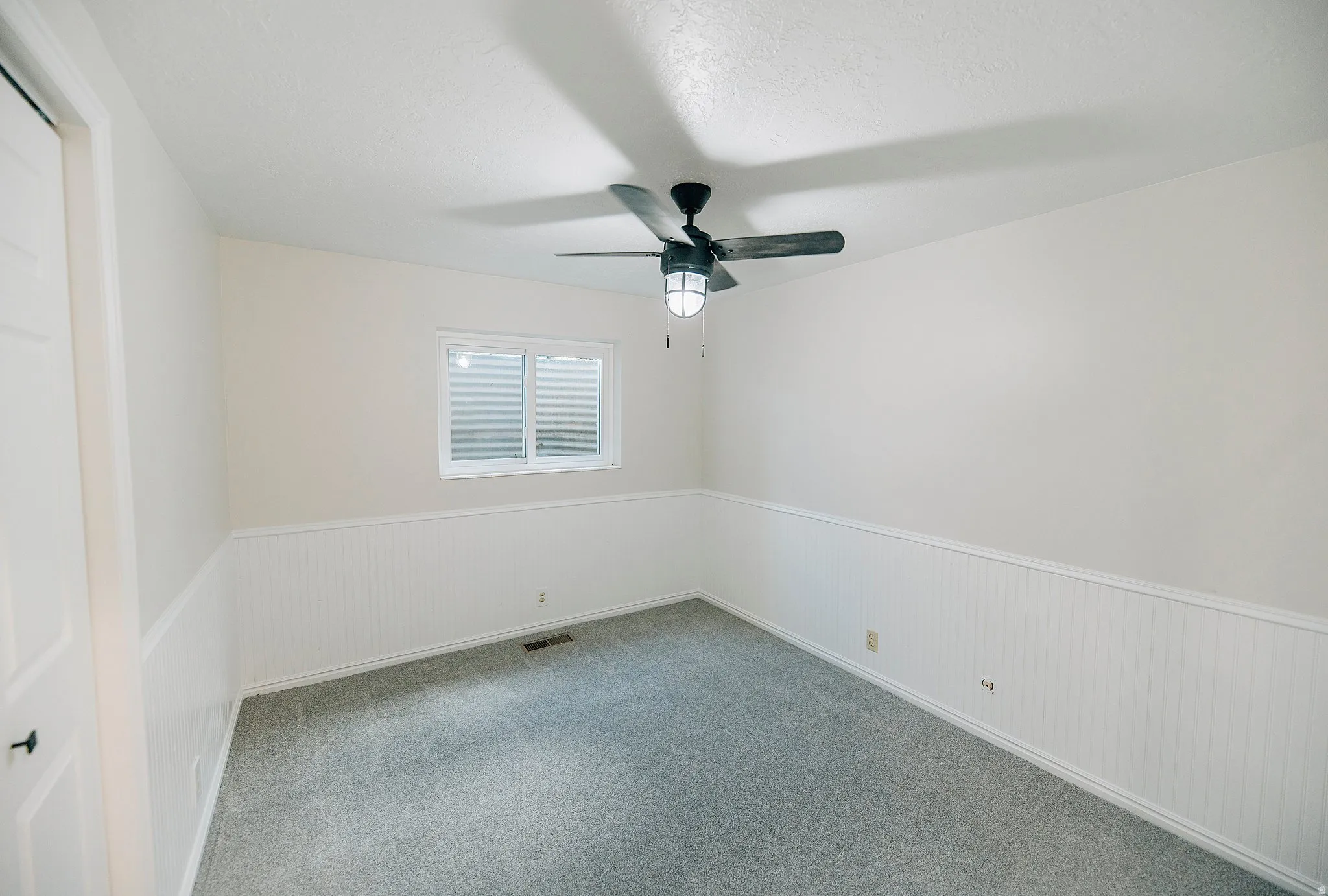 Carpeted empty room featuring a wainscoted wall and ceiling fan