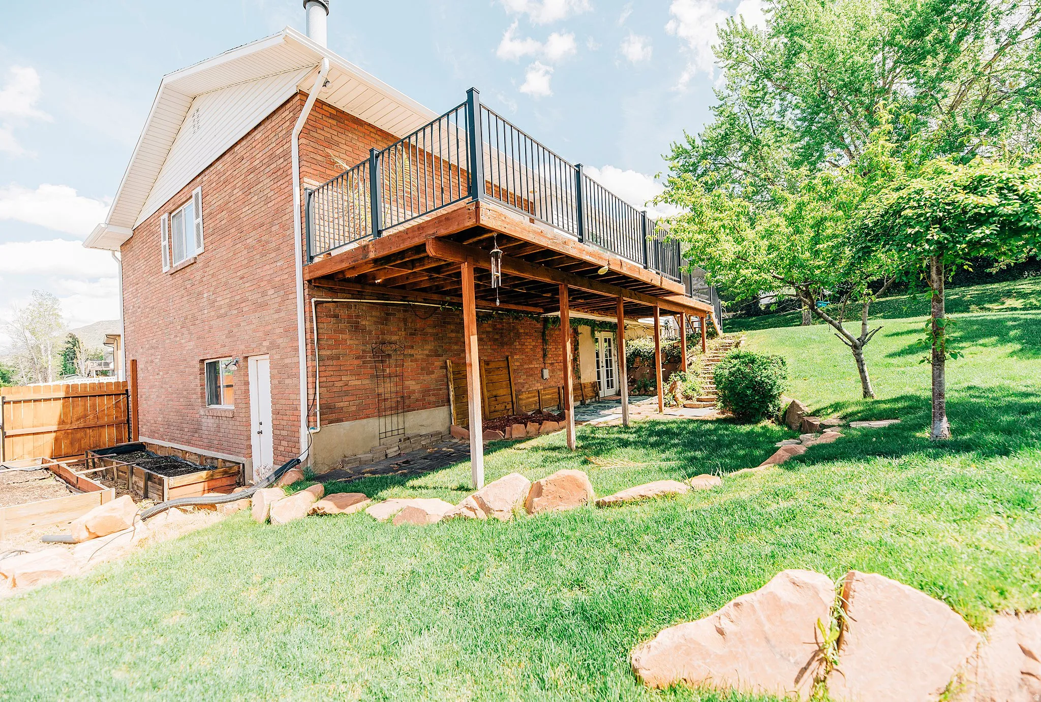 Rear view of house with a deck, a vegetable garden, brick siding, and a lawn
