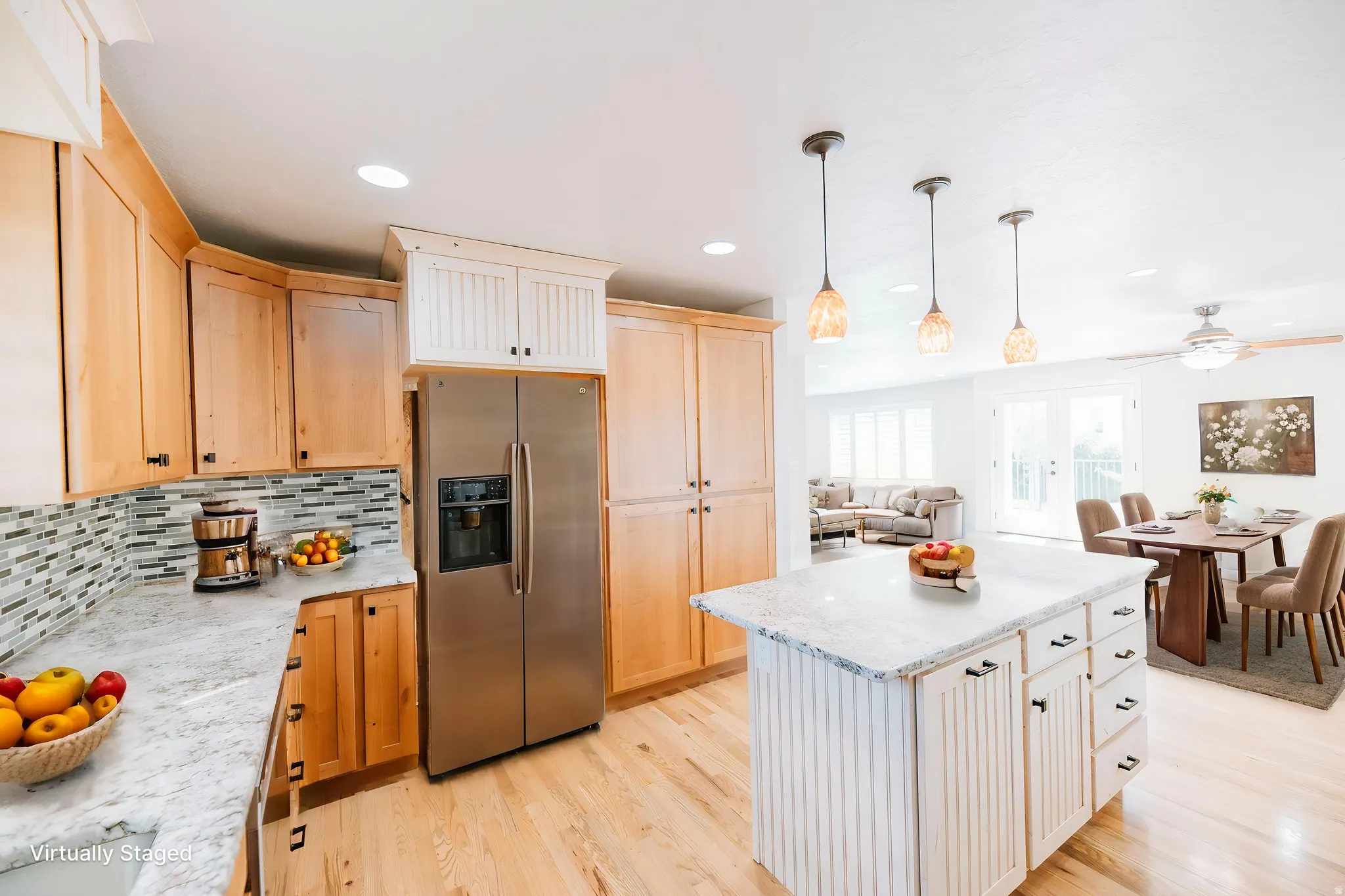 Two tone kitchen featuring stainless steel refrigerator with ice dispenser, light wood-style flooring, light stone countertops, a center island, and open floor plan