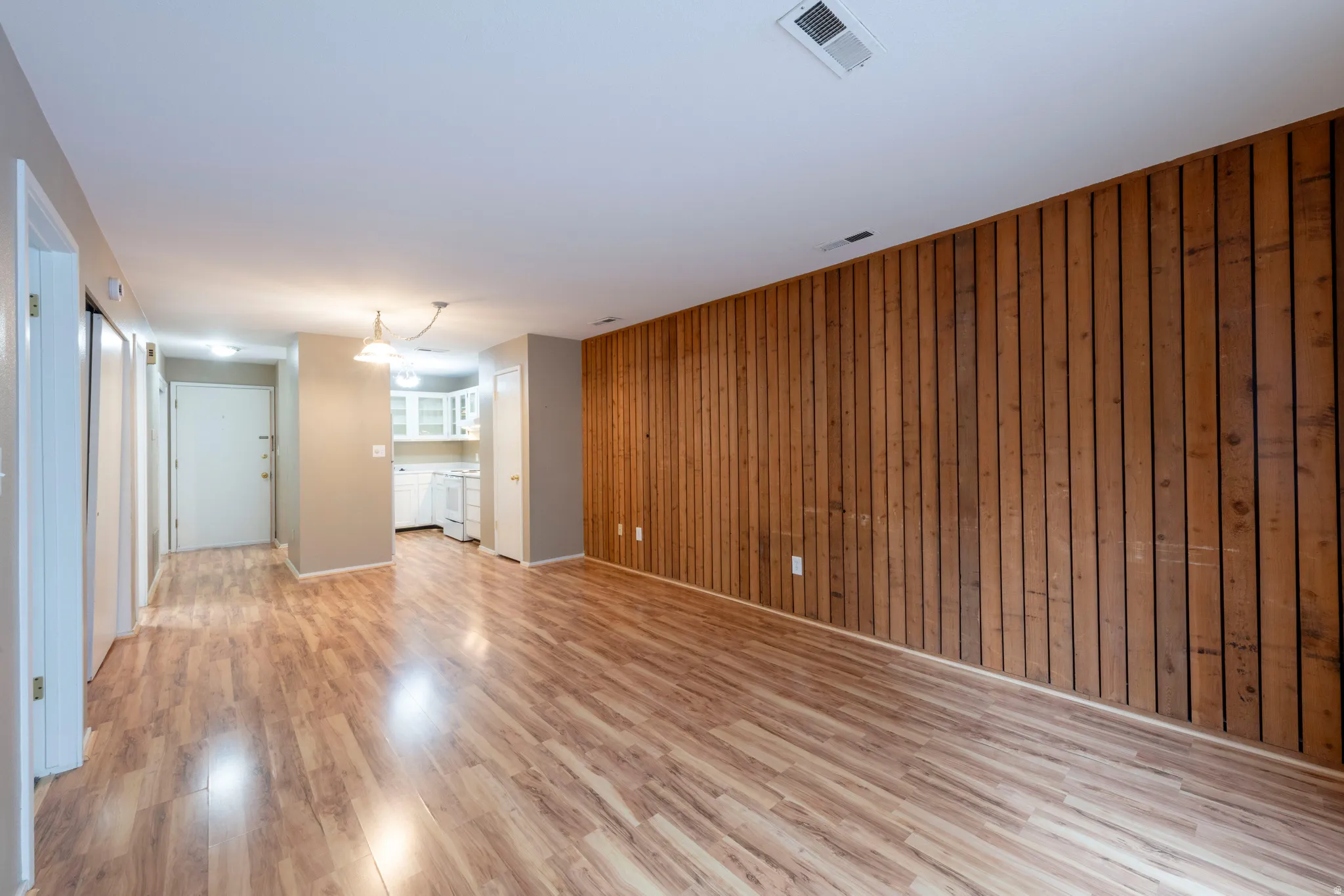 Living area without furniture, light wood-style flooring and wood walls