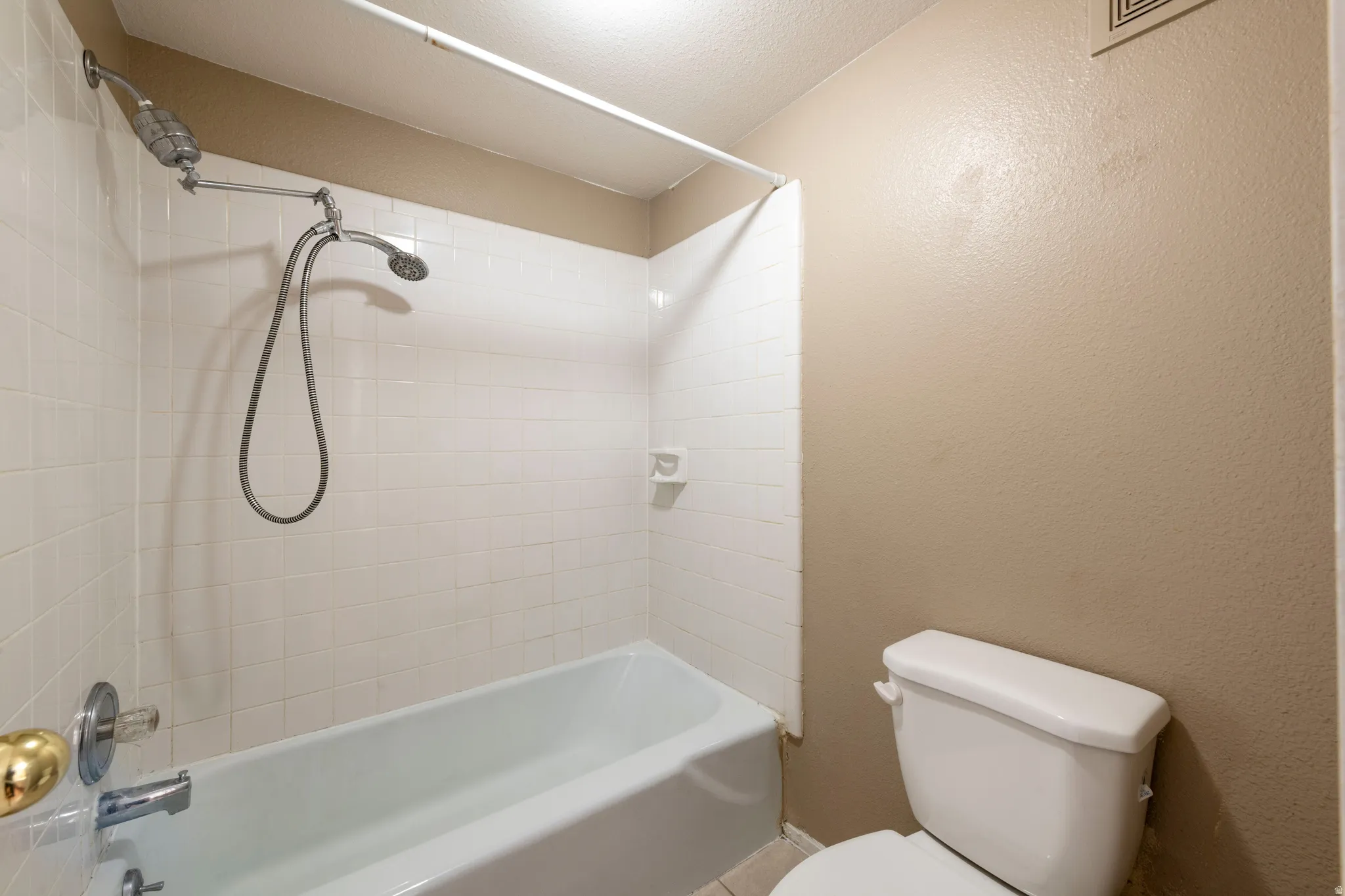 Bathroom featuring washtub / shower combination and a textured wall