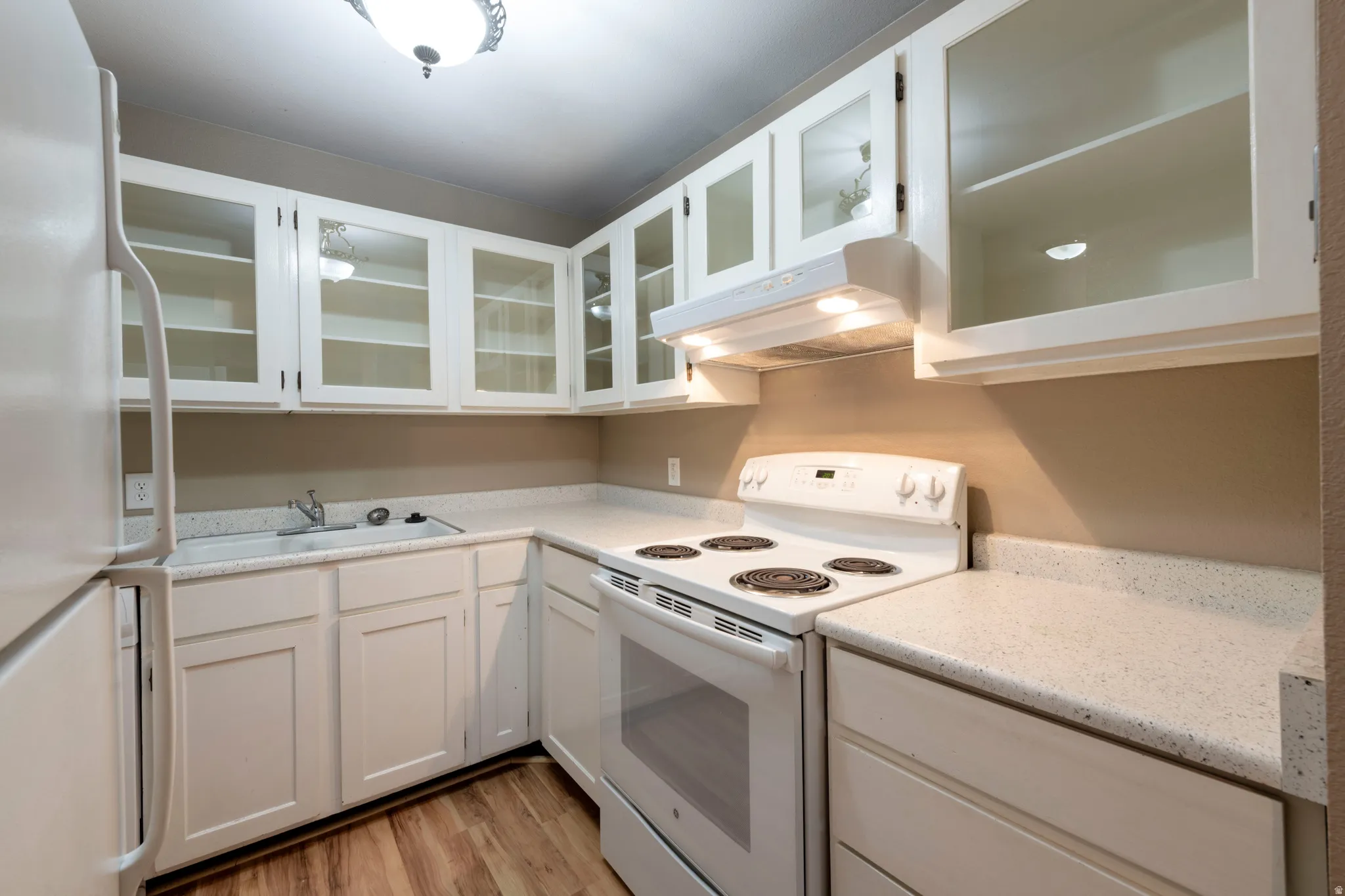 Kitchen with white cabinetry, glass fronted cabinets, white appliances, and light wood-style flooring