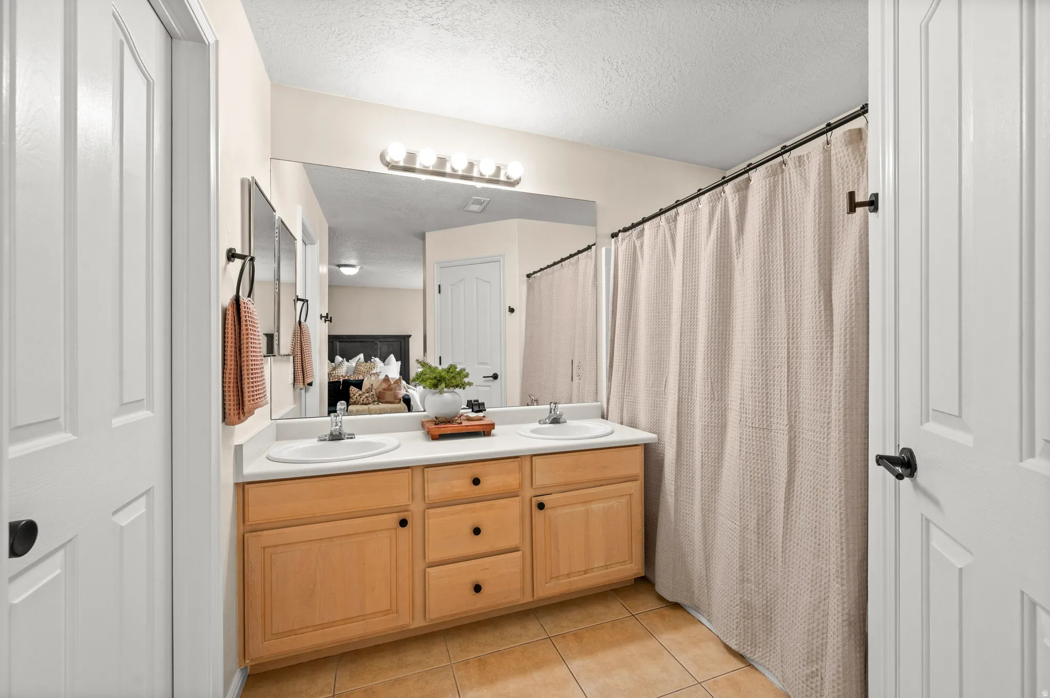 Bathroom with double vanity, light tile patterned floors, curtained shower, and a textured ceiling