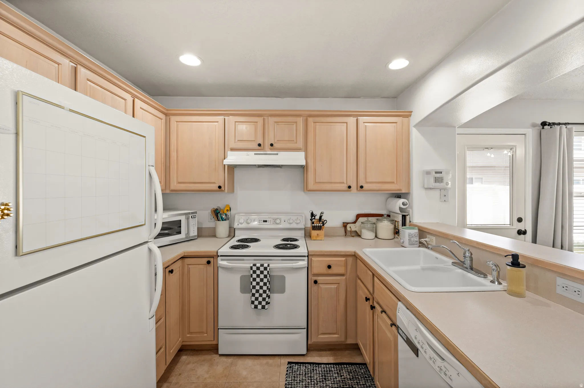 Kitchen featuring white appliances, light wood finish cabinets, light countertops, a peninsula, and recessed lighting