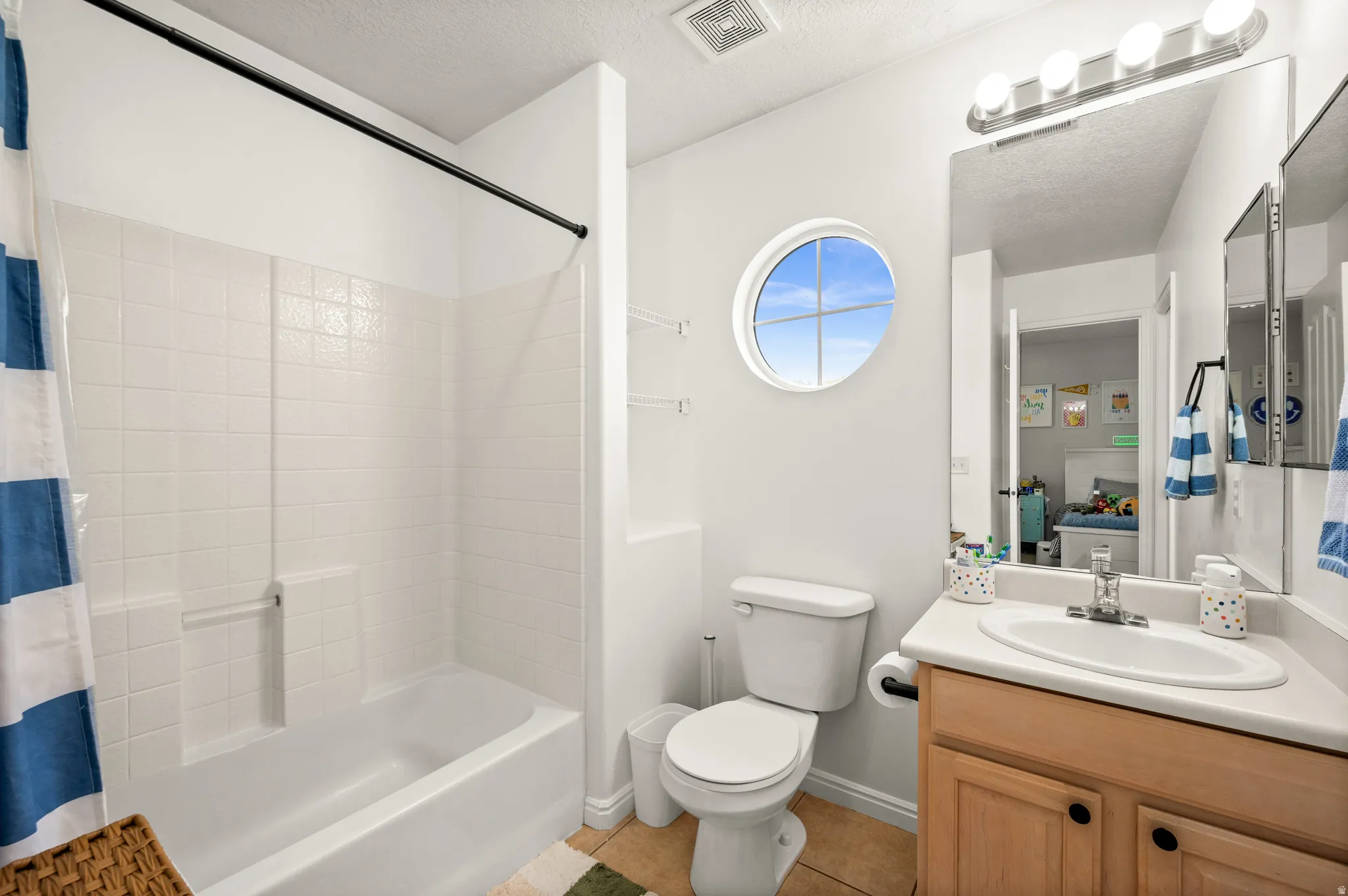 Bathroom with vanity, light tile patterned flooring, a textured ceiling, and shower / tub combo