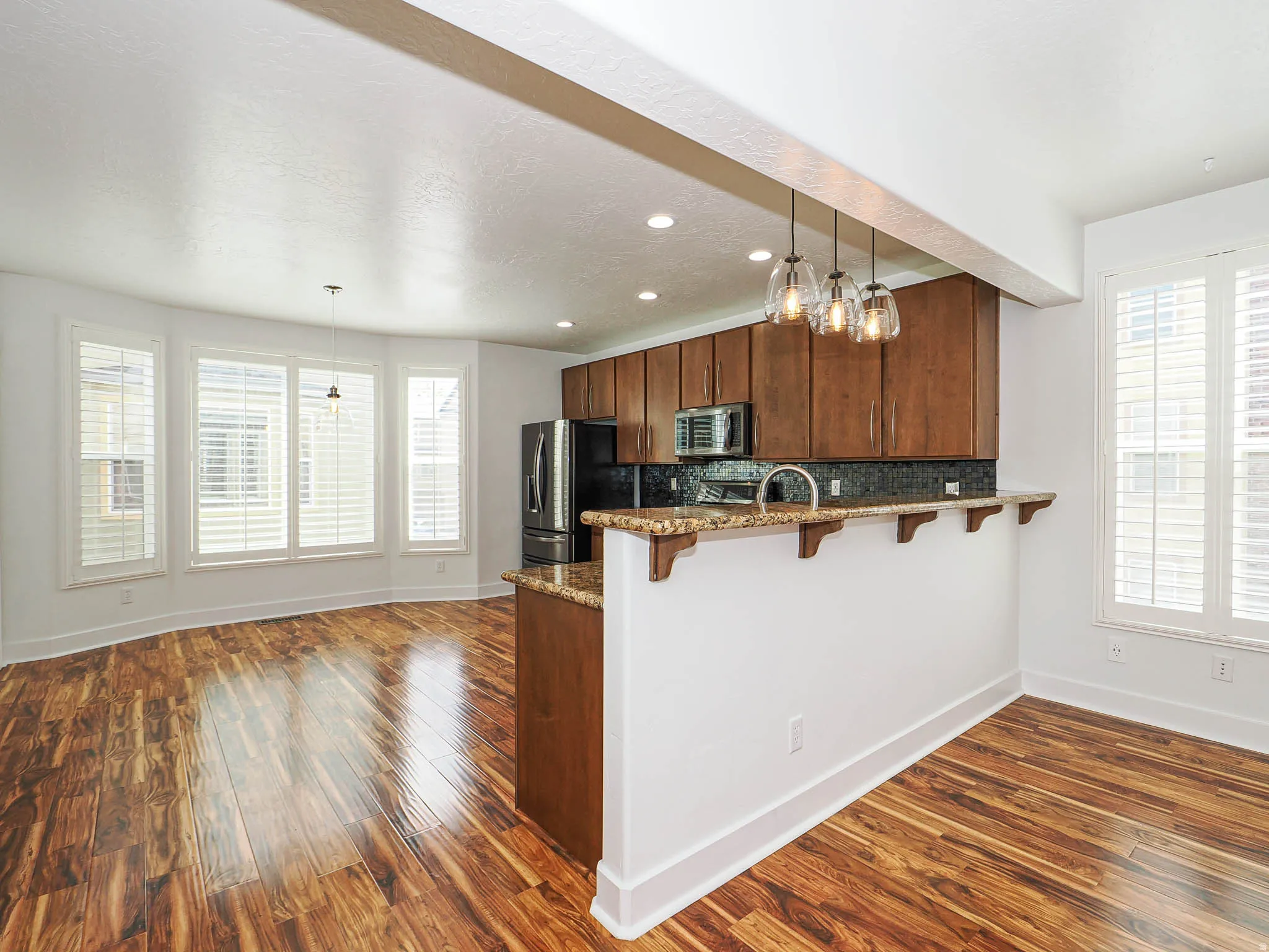 Kitchen featuring dark stone countertops, a peninsula, a kitchen breakfast bar, decorative backsplash, and dark wood finished floors