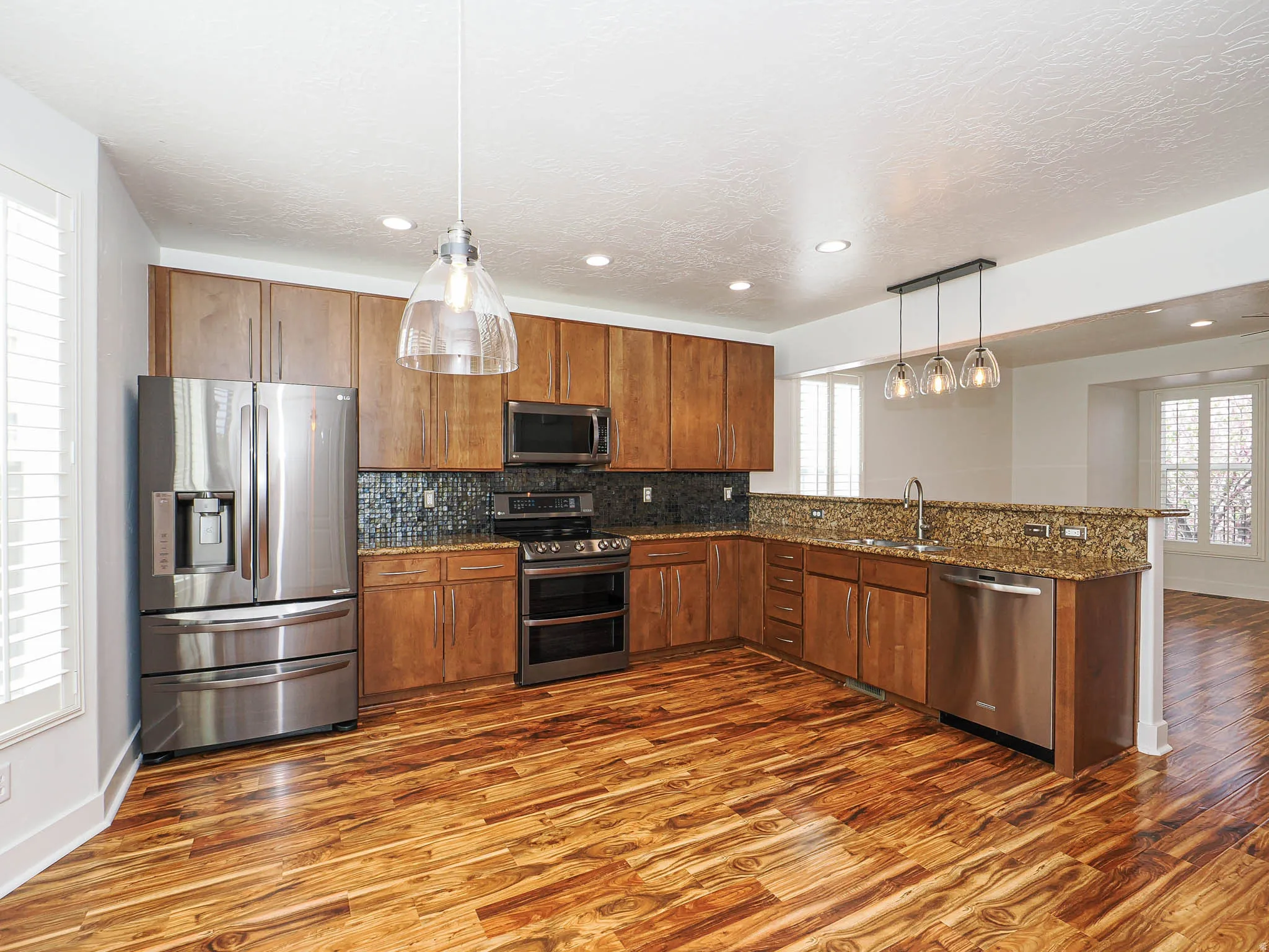 Kitchen featuring plenty of natural light, stainless steel appliances, dark stone counters, decorative light fixtures, and a textured ceiling