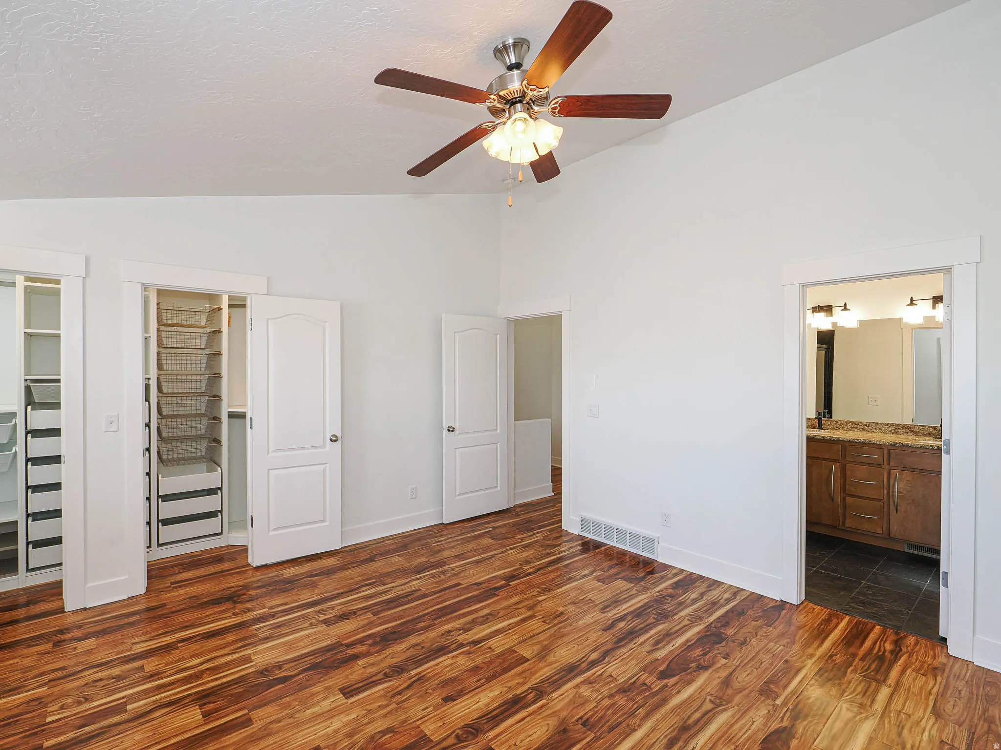 Unfurnished bedroom featuring vaulted ceiling, ensuite bathroom, dark wood finished floors, and ceiling fan