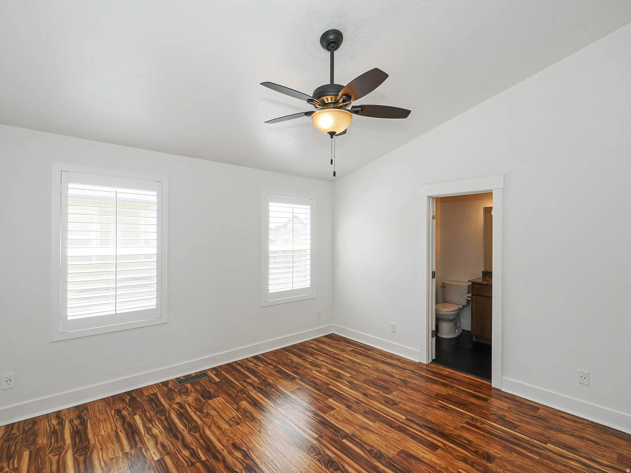 Empty room with dark wood-type flooring, vaulted ceiling, and a ceiling fan